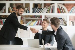 MSP resources Businessman greeting congratulating new smiling executive team member or making deal with handshake at conference table, friendly company ceo shaking partners hand welcoming at meeting among three